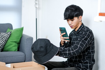 Serious Young Person Sits On The Floor Using His Smartphone To Capture Image Of New Bucket Hat