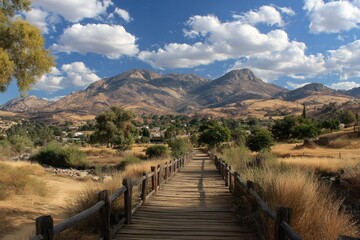 Wooden bridge leading to a valley nestled between mountains under a partly cloudy sky