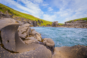 Glacial river waters carve through smooth volcanic rocks in Iceland surrounded by bright green...
