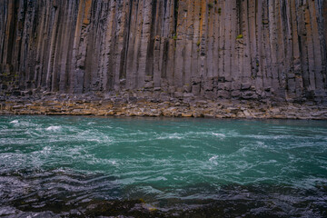 Turquoise glacial waters flow past towering basalt columns in Stuðlagil canyon Iceland showcasing...