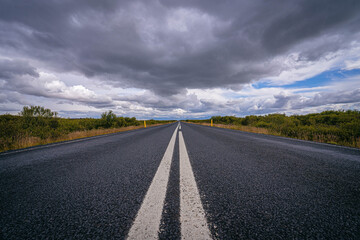 An endless Icelandic road stretches into the horizon beneath brooding storm clouds, a cinematic path through untamed wilderness and open skies