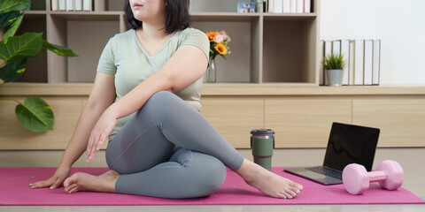 Inclusive Wellness. Young woman practicing yoga and stretching at home with laptop and dumbbells.