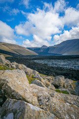 Volcanic rocks frame a sweeping view of Iceland&rsquo;s highlands, where dark lava fields stretch toward distant glacial valleys under a sky of shifting clouds