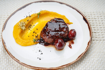 Meat in plum sauce with mousse in a plate on a white background