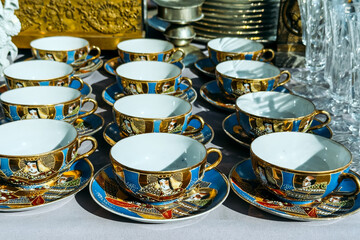 Close-up of ornate porcelain tea cups and saucers with gold details and hand-painted portraits....