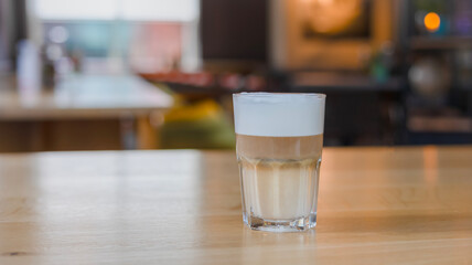 Close-up of a hot latte macchiato in a tall transparent glass, resting on a wooden table in a cozy...