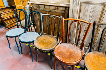 Assorted secondhand wooden chairs arranged in a row inside a vintage furniture store. Circular economy, sustainable furniture, reuse economy, eco-conscious living