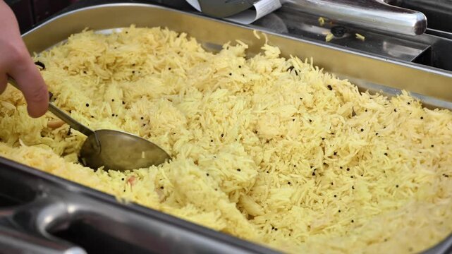 Chef serving indian saffron rice with metal spoon in buffet tray