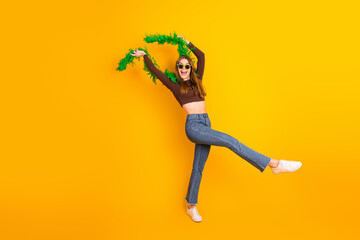 Cheerful young woman with a vibrant yellow background posing creatively with a green boa accessory showcasing casual fashion and happiness