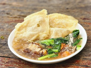 Thai crispy noodle rad na with pork belly, kale, and gravy sauce served in a white bowl on rustic...