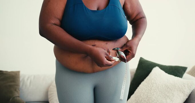 Curvy black woman checks waist circumference with measuring tape