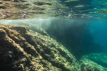 An awe-inspiring underwater landscape with a rocky reef illuminated by beautiful sunbeams filtering through the clear turquoise sea surface.