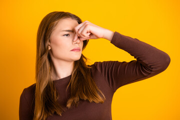 Young woman holding her nose with obvious displeasure standing against a vibrantly yellow...