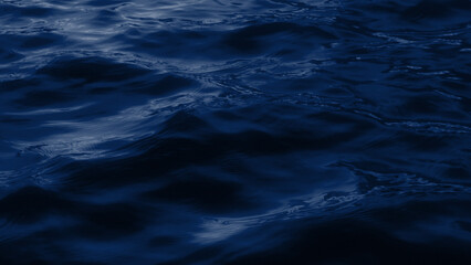 A dark, moody, close-up shot of deep blue sea waves under a dark sky. The low-angle perspective...