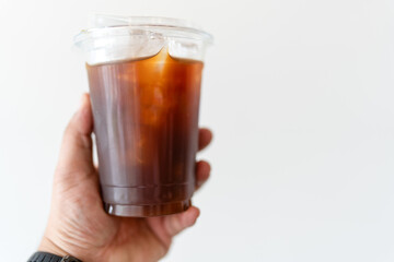 Hand holding a plain plastic takeaway cup of cold Americano against white background