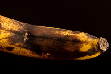 old overripe banana blackened during storage on a black pine board, blackened rotting banana on a...