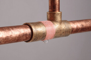 A copper water pipe exhibits a band aid wrapped around a joint, indicating a temporary fix for a small leak in a residential environment