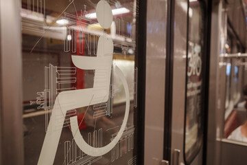 A close-up photograph of the white wheelchair accessibility symbol on a glass door inside a public transport train.