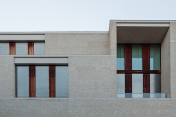 The clean, geometric facade of a modern minimalist building, featuring a layered composition of light-colored brick, large windows, and a recessed balcony.
