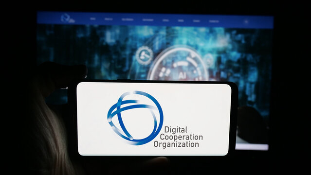 Stuttgart, Germany - 08-28-2025: Person holding cellphone with logo of Digital Cooperation Organization (DCO) on screen in front of webpage. Focus on phone display.