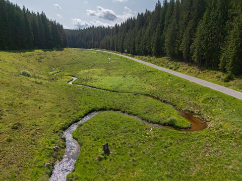 Aerial view of a meandering stream cutting through vibrant green meadows, bordered by a dense forest and a thin road, Sihla, Bansk&Atilde;&iexcl; Bystrica Region, Slovakia.