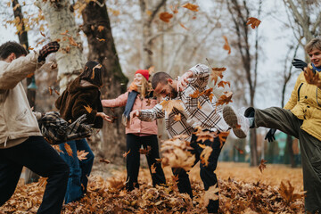 A joyful group of friends playfully throwing autumn leaves in a park surrounded by trees, capturing the fun and warmth of the season.