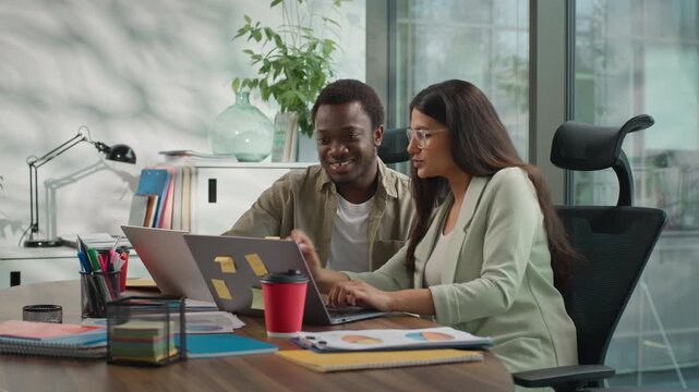 Two multiethnic business people informal team in office working laptop talking African American businessman Hindu businesswoman looking computer monitor male mentor helping female intern assistance