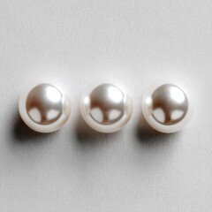 Three lustrous white pearls, smooth and round, sit in a horizontal row against a light gray background