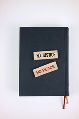 Wooden message blocks displaying the phrases 'No Justice' and 'No Peace' placed on a dark book, emphasizing themes of equality and the drive for fairness