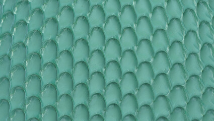 Fototapeta premium The image features a close-up of a textured surface displaying overlapping scales in a vibrant turquoise color, illuminated softly. This artistic design highlights intricate details