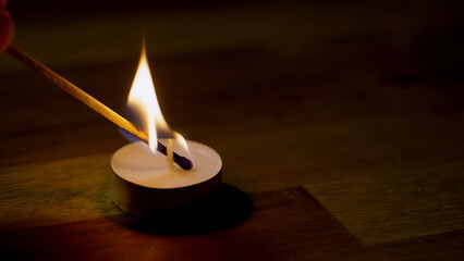 A hand ignites a candle using a match stick in a dimly lit room, creating a warm and inviting...