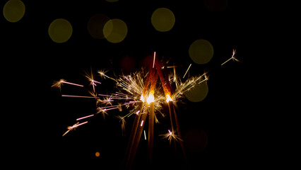 Bright sparks shoot from multiple sparklers held together during a night celebration, creating a...