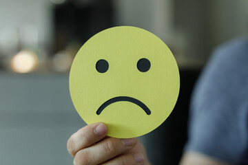 Close-up of a hand holding a yellow sad face emoji.  Represents sadness, depression, or unhappiness.