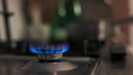 A blue flame ignites on a gas stove in a cozy kitchen, illuminating the surroundings with a warm glow.