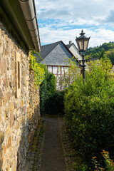 Winding path through a quaint village lined with stone walls and greenery under a bright sky