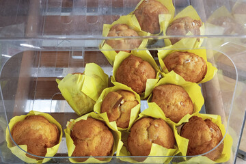 Muffins wrapped in yellow paper packaging on display in a pastry shop.