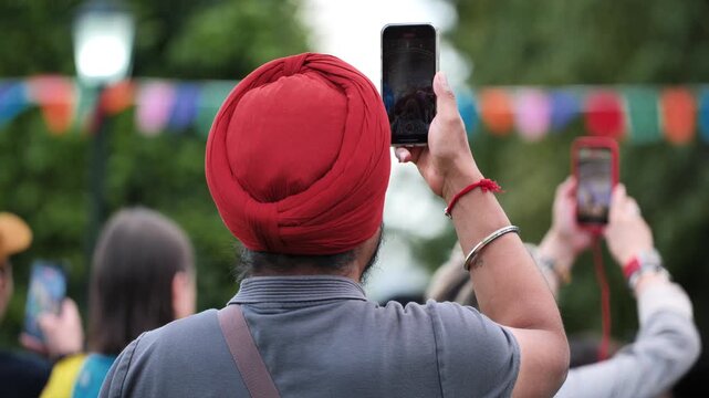Man Sikh with red turban recording parade with smartphone in India