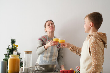 Woman and a boy toast with glasses of orange juice in a bright kitchen. They appear joyful and...