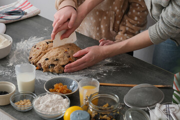 Two individuals are working together to knead a rich, fruit-filled dough on a gray countertop....