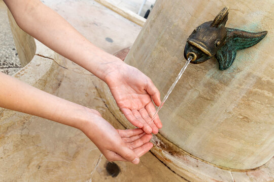 Hands collecting water from dolphin fountain. Close-up of hands gathering clean water from a decorative dolphin-shaped fountain spout, symbolizing refreshment and public water access. - Powered by Adobe