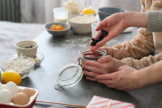 Two people are collaborating in a kitchen, adding ingredients to a glass jar. Flour, eggs, and fruits are arranged on the countertop, highlighting the baking process.