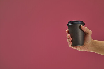Hand holding a disposable coffee cup with black lid on a pink background, ideal for showcasing...