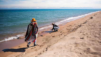 Two sisters are walking along the beach on a sunny day. The woman is wearing a cowboy hat and a poncho. Tourism, adventure and freedom