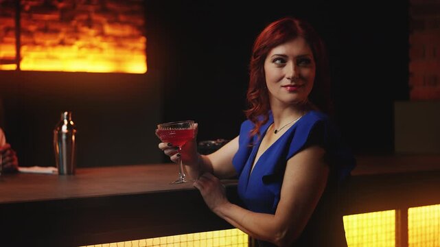 Attractive red-haired woman drinking cocktail and looking for date at night bar