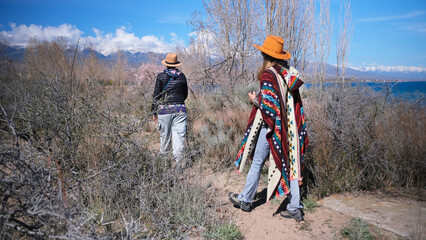 Obraz premium Two women are walking through a field overgrown with dry bushes. Two friends are walking near the blue lake. Travel and adventures