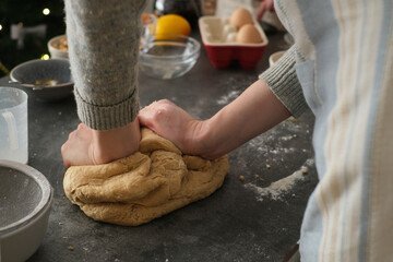 A person kneads dough on a clean countertop, surrounded by various baking ingredients like flour,...