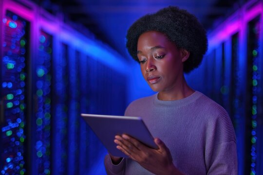 Engaged woman examines data on tablet in a modern server room illuminated with colorful lights