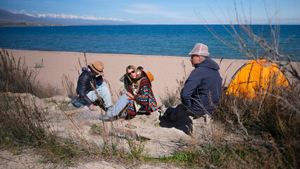 There are three people sitting on the beach next to the tent. A man and his daughters are relaxing...
