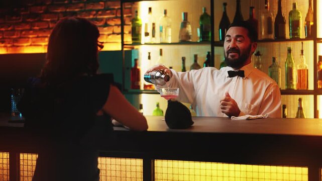 Smiling bartender pouring cocktail and talking with female guest at bar counter