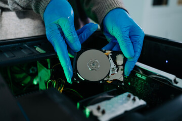 Closeup of gloved technician holding exposed hard drive above desktop PC. Ideal for data recovery,...